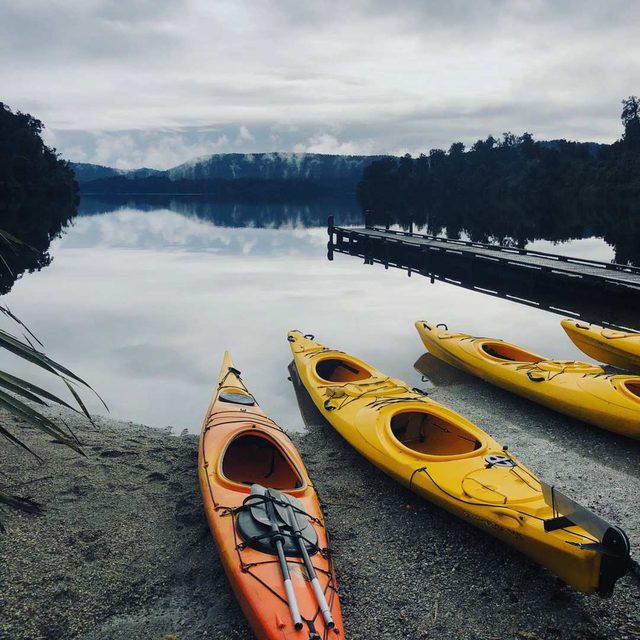 Kayaks resting beside a jetty on a still New Zealand lake under low cloud